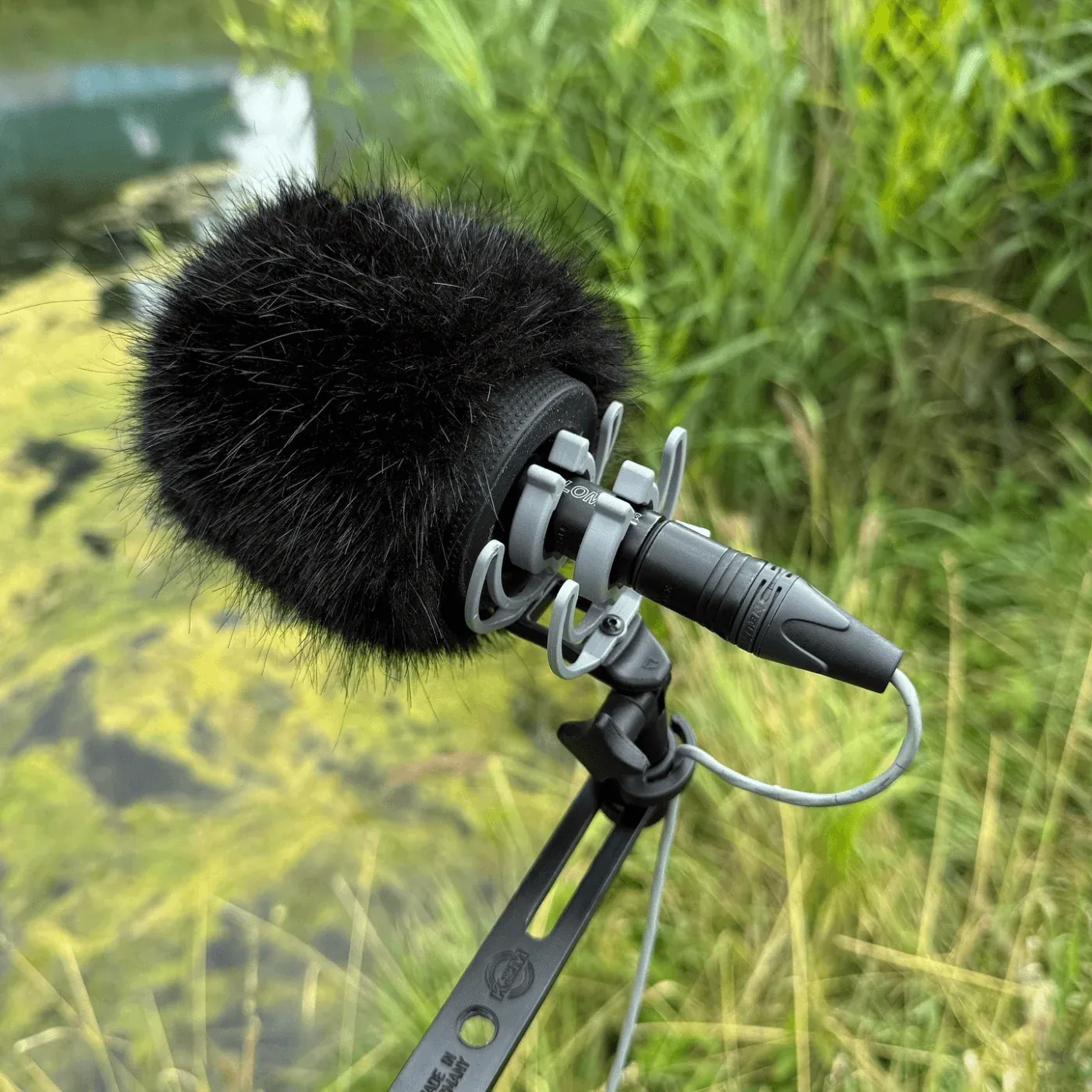 Bubblebee Industries The Windkiller: A Windkiller on a mic in a stand among tall grass.