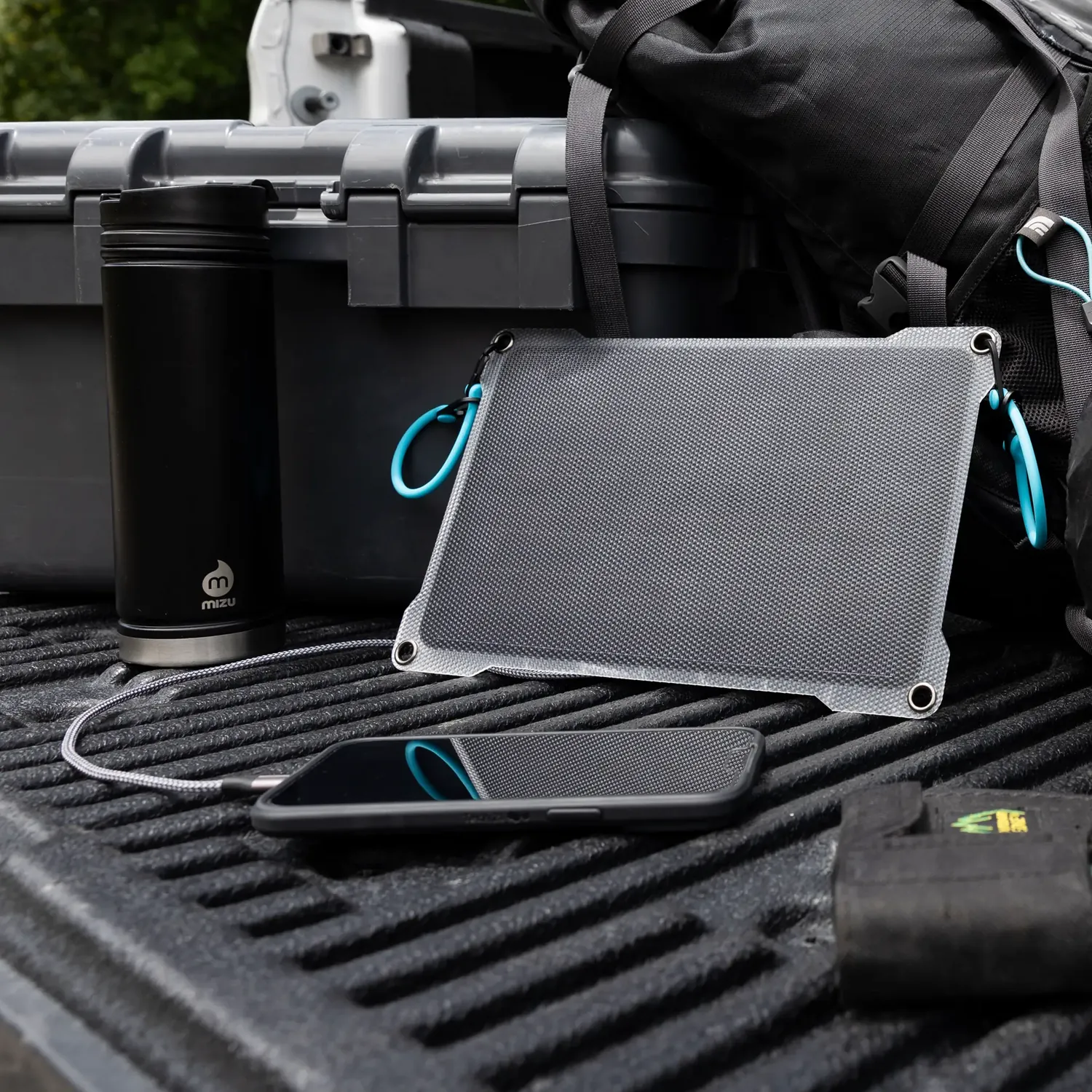Paleblue Approach 1 Single-Panel Solar Charger lying on a truck bed in the sun, charging a phone beside a backpack.