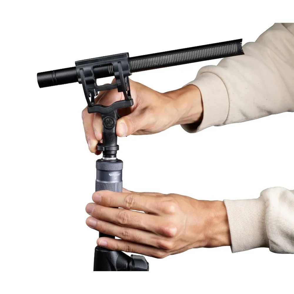 Rycote PCS Spigot on a microphone stand as two hands attach a shotgun mic in its suspension mount.